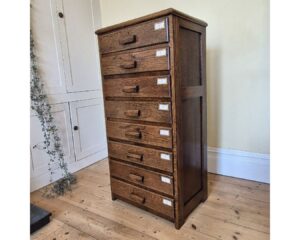 A 1930s flight of oak drawers, each of which retains its original oak pull handle and label holder.